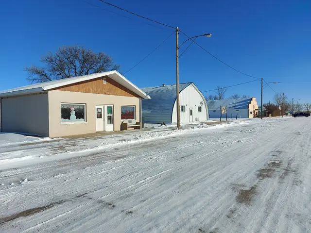 Snowy main street with shops and a quonset building